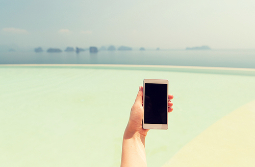 technology, travel, tourism, communication and people concept - close up of male hand holding smartphone with blank screen on summer beach