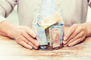 savings, money, annuity insurance, retirement and people concept - close up of senior woman hands with money in glass jar