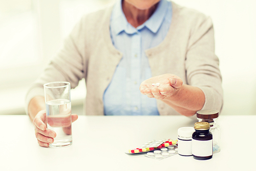 age, medicine, health care and people concept - close up of senior woman with pills and glass of water at home