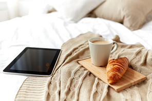 technology, coziness, morning and winter concept - tablet pc computer, coffee cup and croissant on bed at home