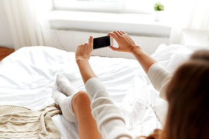 technology, winter, augmented rality and people concept - young woman in bed holding smartphone with black empty screen photographing at home bedroom