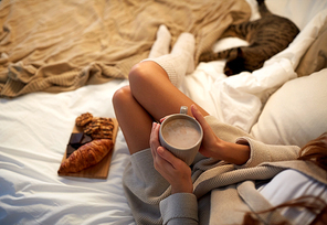 winter, coziness, leisure and people concept - close up of young woman with cup of coffee or cacao and sweets in bed at home