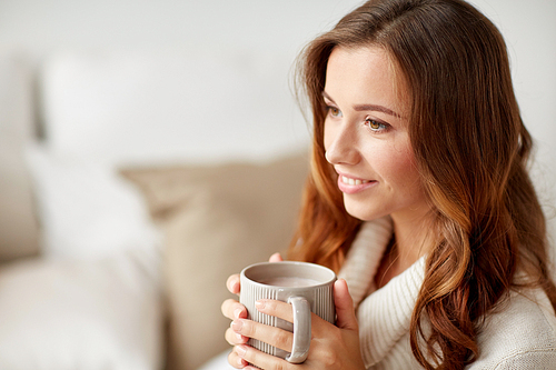 leisure, drink, winter and people concept - happy young woman with cup of coffee or cocoa at home