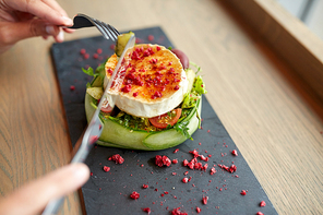 food, culinary, haute cuisine and people concept - woman eating goat cheese salad with vegetables and dried raspberries using fork and knife at restaurant or cafe