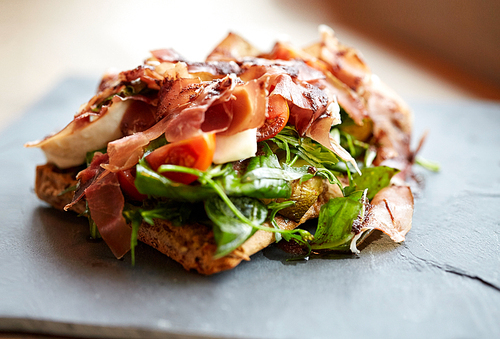 food, dinner, haute cuisine and eating concept - prosciutto ham salad on stone plate at restaurant