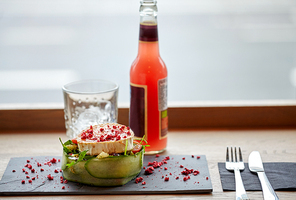 food, eating and object concept - goat cheese salad with vegetables, bottle of drink, glass with ice and cutlery at restaurant or cafe
