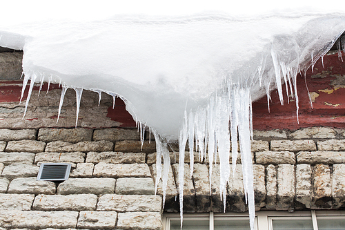 season, housing and winter concept - icicles and snow hanging from building roof