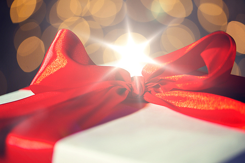 christmas, holidays, presents, new year and celebration concept - close up of gift with red bow over lights background