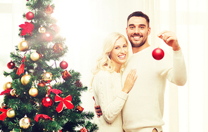family, x-mas, winter holidays and people concept - happy couple decorating christmas tree with ball at home