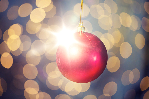 christmas, decoration, holidays concept - close up of red shiny ball over golden lights background