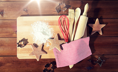 baking, cooking, christmas and food concept - close up of gingerbread cookies, molds with flour and kitchenware set on wooden cutting board at home kitchen from top