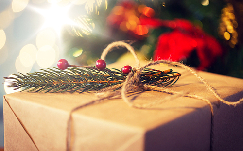 christmas, holidays, presents, new year and decor concept - close up of gift box wrapped into brown mail paper and decorated with fir brunch and rope bow over lights background