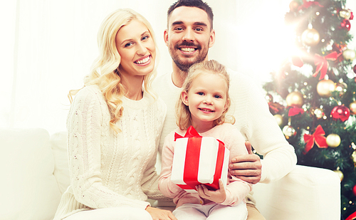 family, christmas, holidays and people concept - happy mother, father and little daughter with gift box sitting on sofa at home