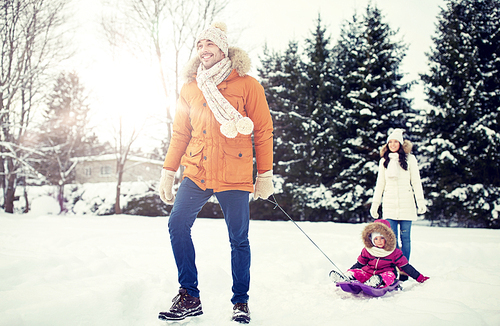 parenthood, fashion, season and people concept - happy family with child on sled walking in winter outdoors