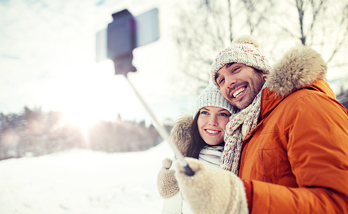 people, season, love, technology and leisure concept - happy couple taking picture with smartphone selfie stick on over winter background