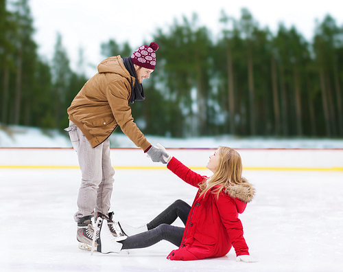 people, sport and leisure concept - smiling man helping women to rise up on skating rink over winter outdoor background