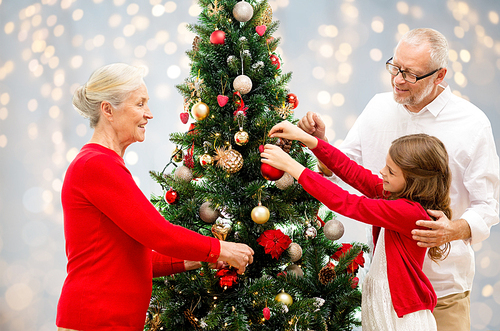winter holidays, family and people concept - happy grandparents and granddaughter decorating christmas tree over lights background