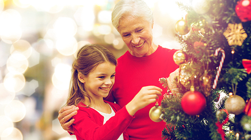 winter holidays, family and people concept - happy grandmother and granddaughter decorating christmas tree over lights background
