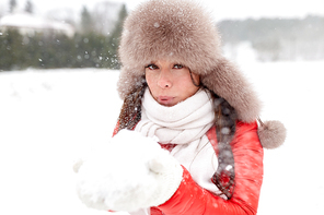 people, season and leisure concept - happy woman in winter fur hat blowing on snow in her hands outdoors