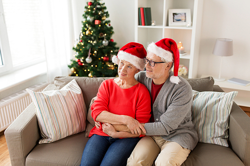 christmas, holidays and people concept - happy smiling senior couple in santa hats at home