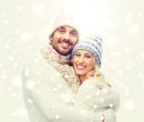 winter, love, couple, christmas and people concept - smiling man and woman in hats and scarf hugging