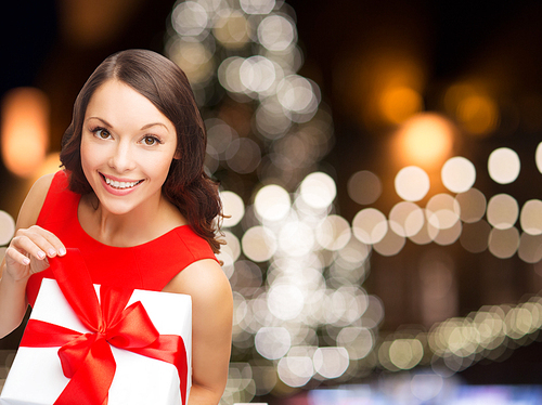christmas, holidays and people concept - smiling woman in red dress with gift box over lights background