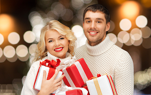 christmas, holidays and new year concept - happy family couple in sweaters holding gifts or presents over lights background