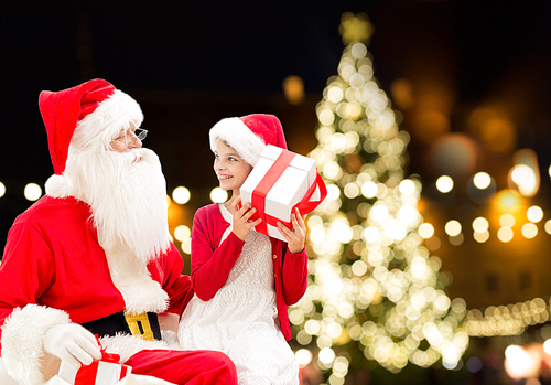 holidays and people concept - santa claus and happy little girl with gift box over christmas tree lights background