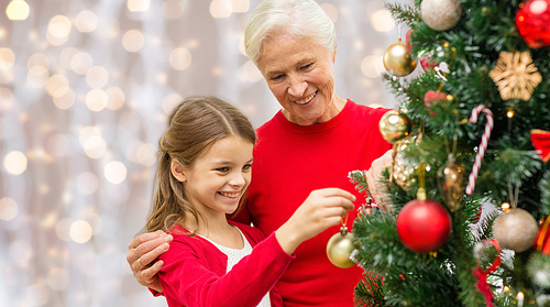 winter holidays, family and people concept - happy grandmother and granddaughter decorating christmas tree over lights background