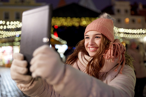 winter holidays and people concept - happy woman with tablet pc taking selfie at christmas tree outdoors