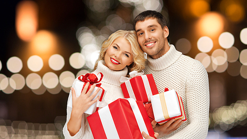 christmas, holidays and new year concept - happy family couple in sweaters holding gifts or presents over lights background