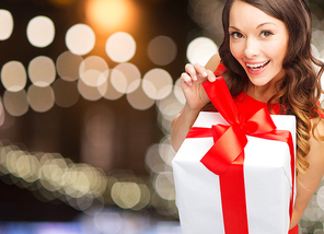 christmas, holidays and people concept - smiling woman in red dress with gift box over lights background