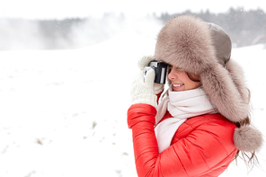people, photography and leisure concept - happy woman in winter fur hat with film camera photographing outdoors