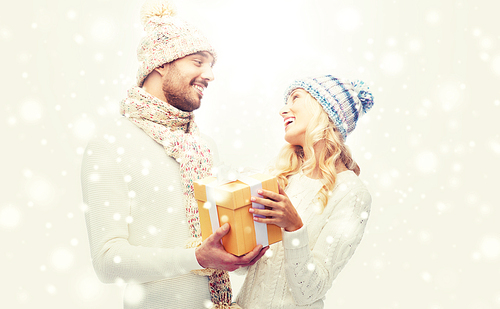 winter, holidays, couple, christmas and people concept - smiling man and woman in hats and scarf with gift box