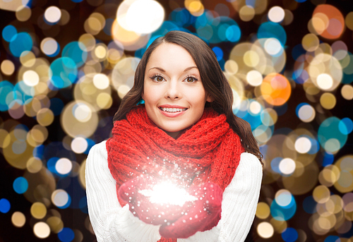 holidays, christmas and people concept - happy woman in scarf and mittens with magic snowflake over lights background