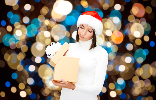 holidays, christmas and people concept - displeased woman in santa hat opening gift box over lights background