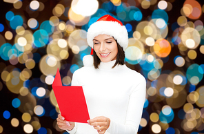 christmas, holidays and people concept - happy smiling woman in santa hat reading greeting card over lights background