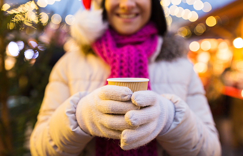 winter holidays, hot drinks and people concept - happy young woman with coffee or mulled wine in cup at christmas market in evening