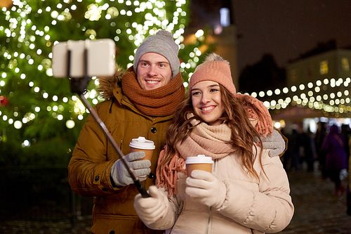 winter holidays, hot drinks and people concept - happy couple with coffee taking selfie in christmas evening