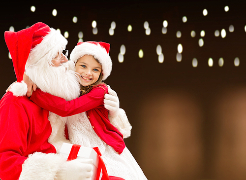 holidays, christmas and people concept - santa claus with gift and happy girl over lights background