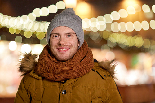 holidays and people concept - portrait of beautiful happy young man over christmas lights in winter evening