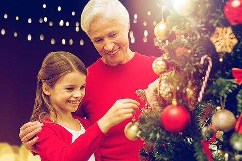 holidays, family and people concept - happy grandmother and granddaughter decorating christmas tree over lights background