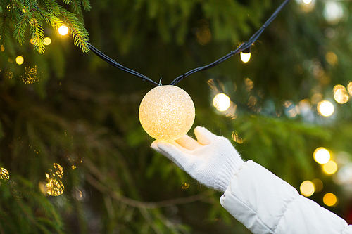 holidays and decoration concept - close up of hand with christmas tree garland bulb outdoors