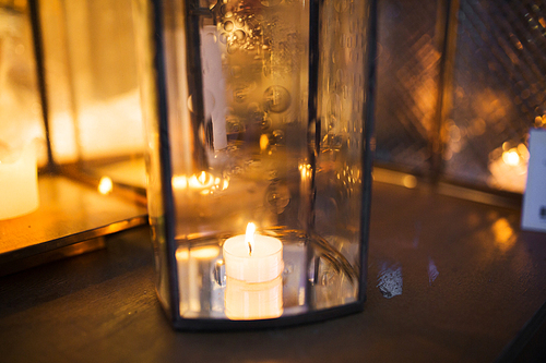 holidays and decoration concept - close up of lantern with candle burning inside