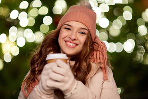 winter holidays, hot drinks and people concept - happy young woman with coffee over christmas tree lights outdoors