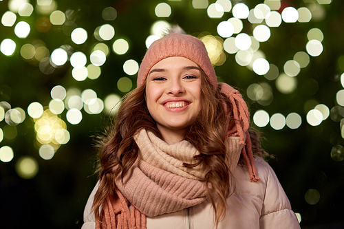 holidays and people concept - portrait of beautiful happy young woman over christmas tree lights in winter evening