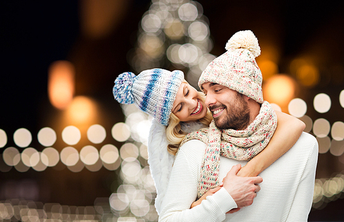 christmas, holidays and people concept - happy couple in hats and scarf hugging over night lights background