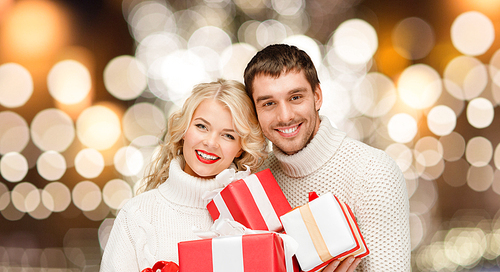 christmas, holidays and new year concept - happy family couple in sweaters holding gifts or presents over lights background