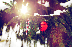 winter holidays and decoration concept - candy cane and christmas ball on fir tree branch covered with snow