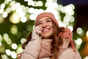 holidays, communication and people concept - portrait of beautiful happy young woman calling on smartphone over christmas tree lights in winter evening